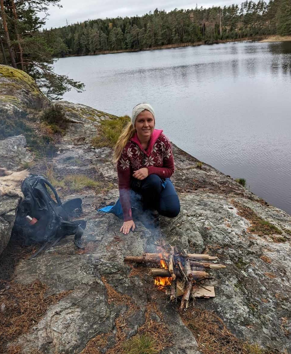 Silvia Sandnes på skogstur, sitter ved vannet med et bål.